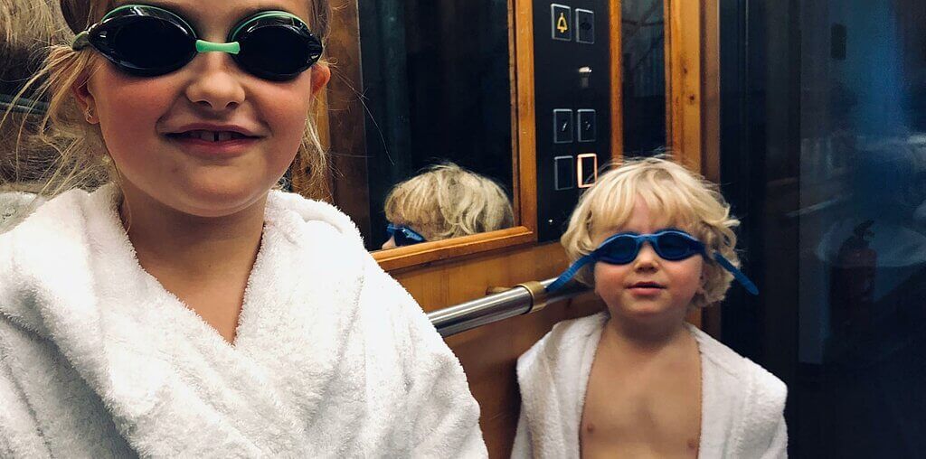 Zwei Kinder im weißen Bademantel und mit Schwimmbrille in einem Aufzug